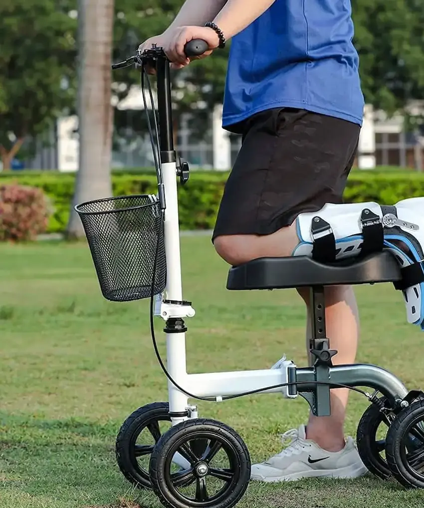 Person using a knee walker scooter with leg support and front basket for mobility aid outdoors.