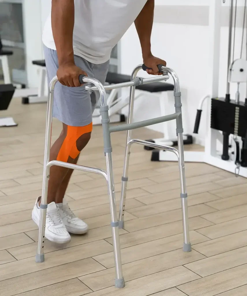 Man using a standard aluminum walker for mobility support during knee injury recovery in a rehabilitation center